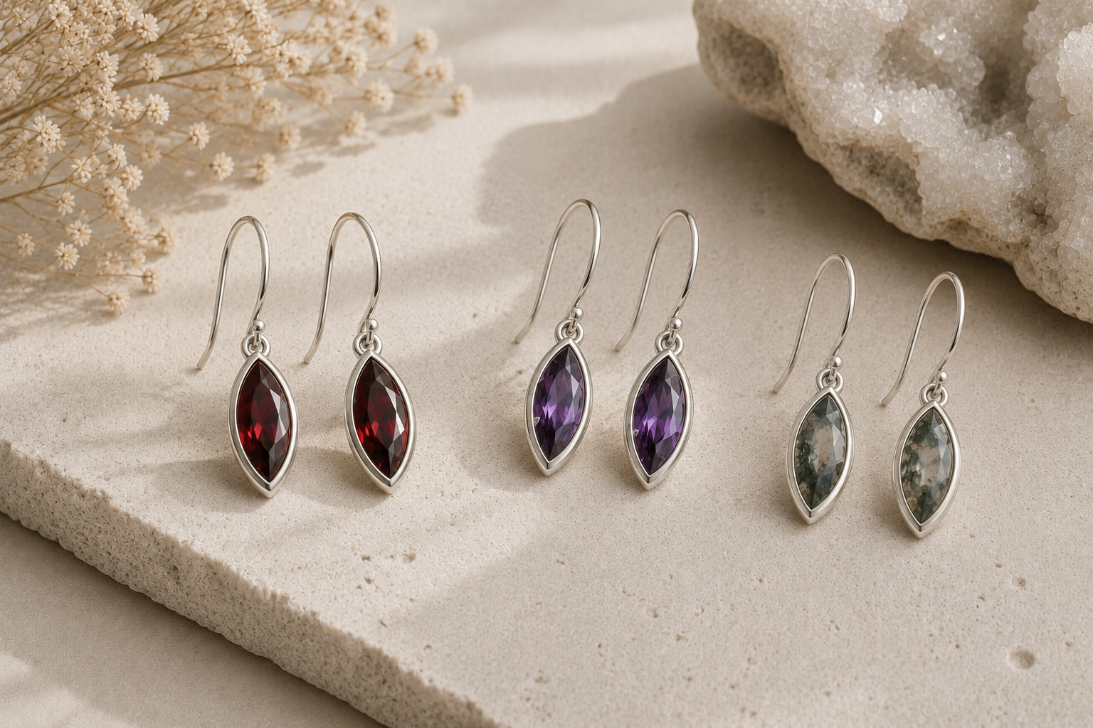 Set of silver earrings with  marquise gemstones on a stone surface with dried flowers.